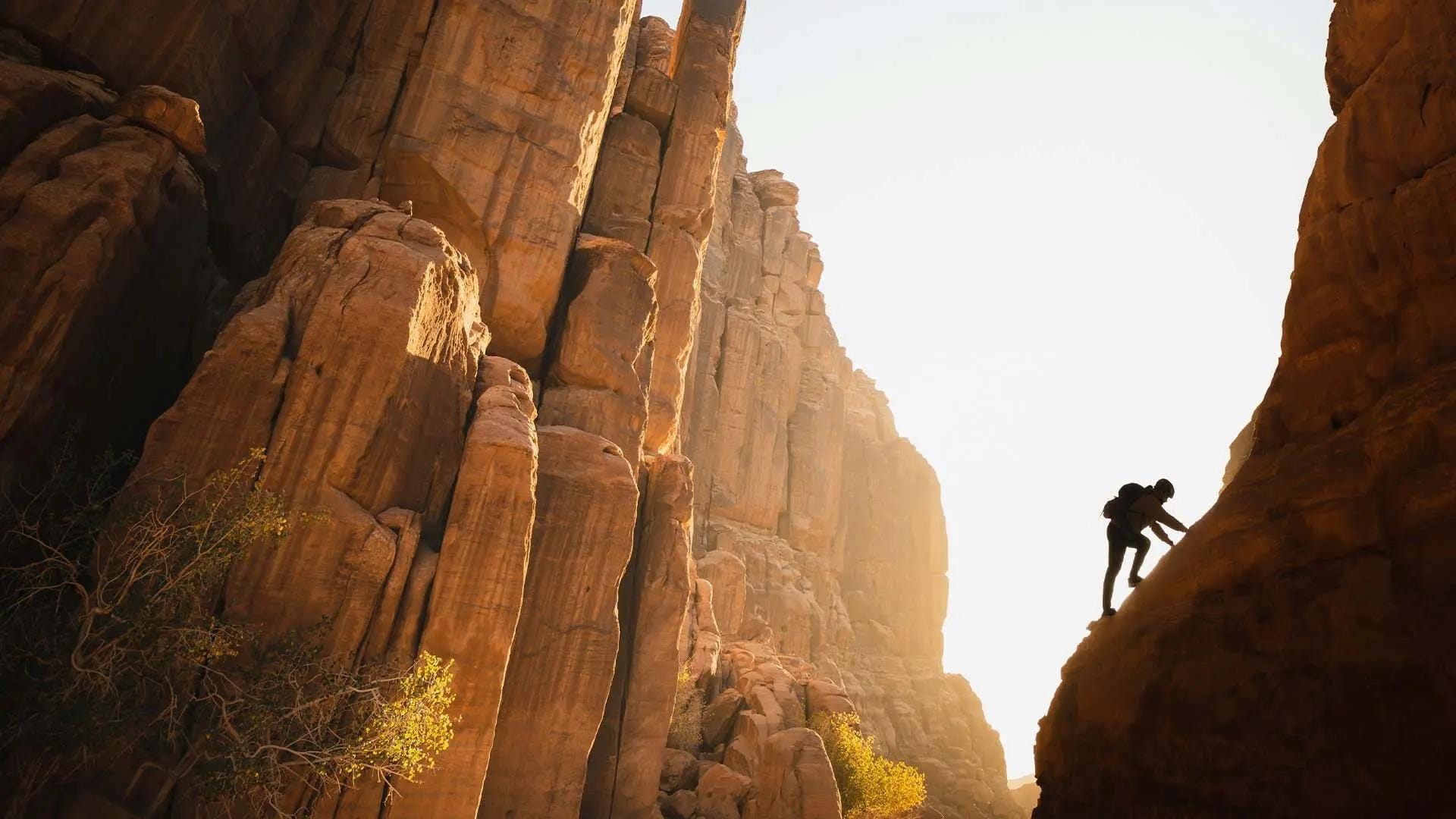 Persona che fa trekking tra alte formazioni rocciose illuminate dal sole.